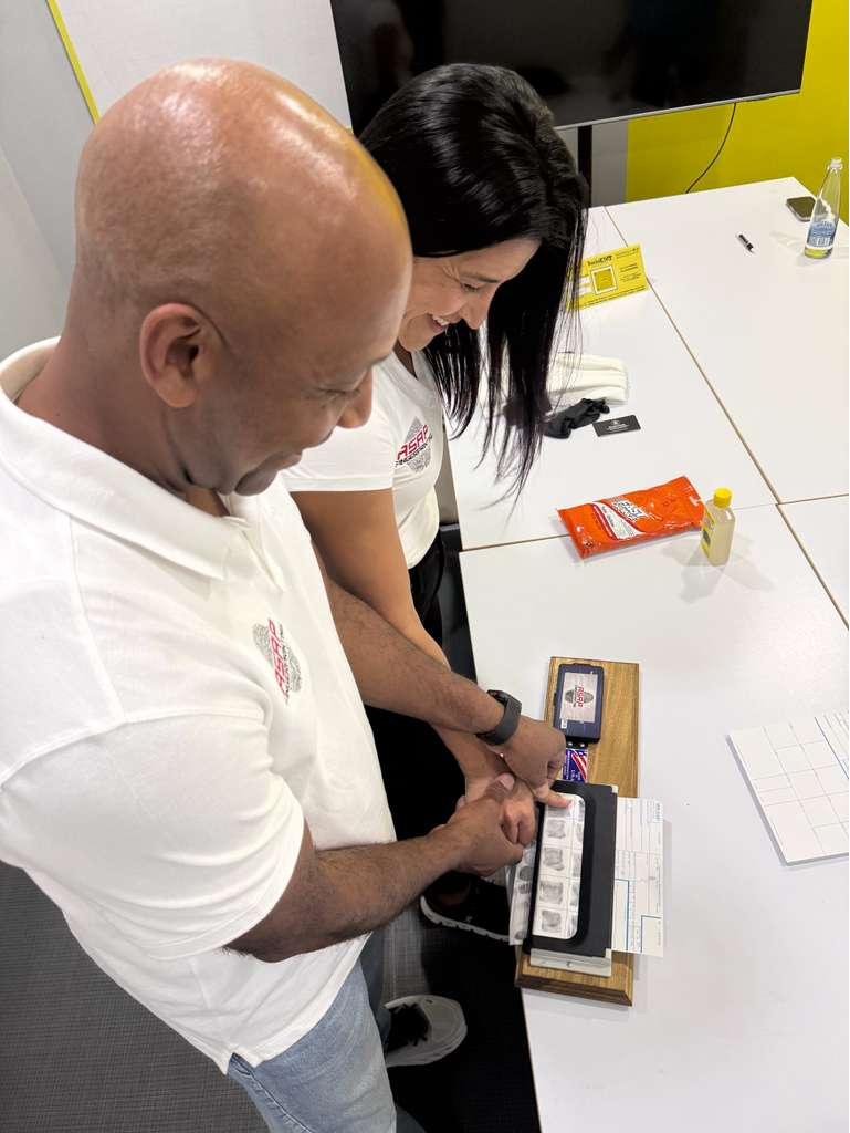 Two ASAP Fingerprinting staff members rolling a client's fingerprints onto a card